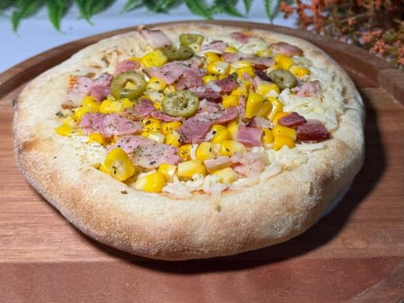 Mini pizza com milho, cubos de bacon e azeitonas sobre uma tábua de madeira